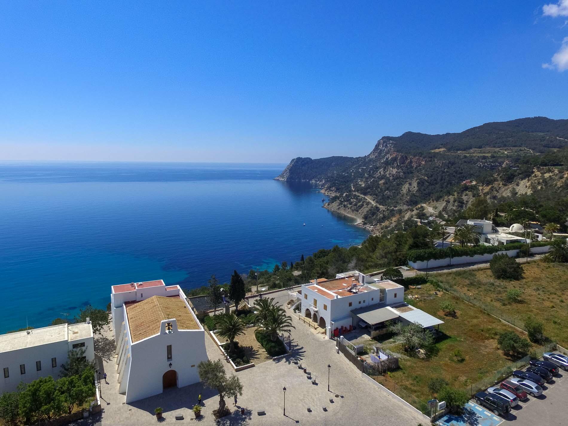 Hooggelegen uitzicht op Es Cubells, Ibiza, met een witgekalkte kerk die uitkijkt over de blauwe zee en de ruige kustlijn