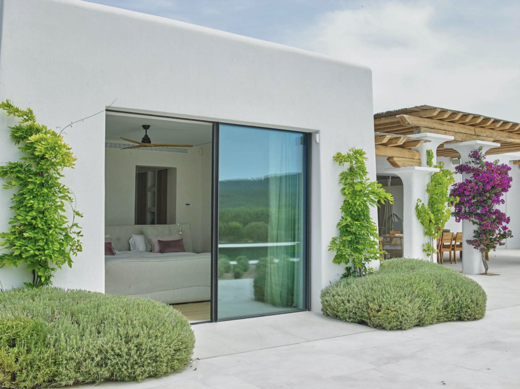 Blakstad villa op Ibiza met witgekalkte muren, glazen schuifdeuren, aangelegde tuin en overdekt terras.